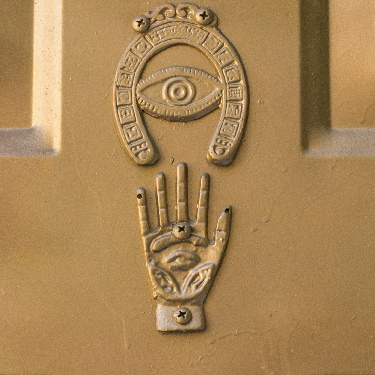 3D Symbol auf Wand in gold. Hand unter einem Auge eingebettet in ein umgekehrtes Hufeisen