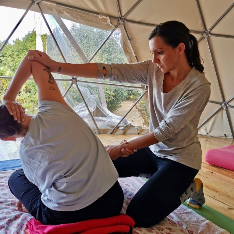Bild von einer Thai Massage. Zwei Frauen, eine sitzt und eine kniet und dehnt die Person seitwärts
